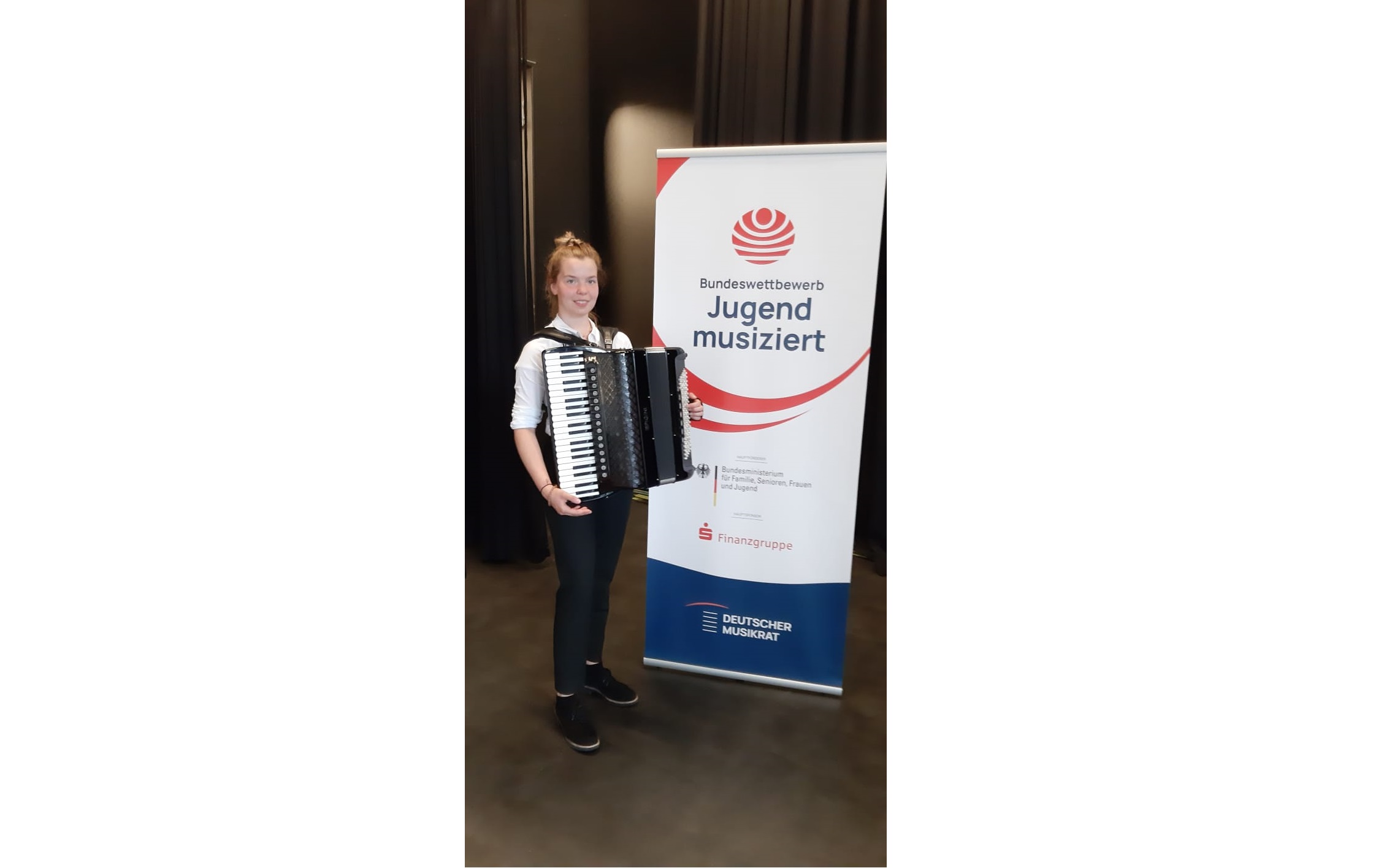Anna-Lena Kreher mit Akkordeon vor dem Banner des Bundeswettbewerbs Jugend musiziert