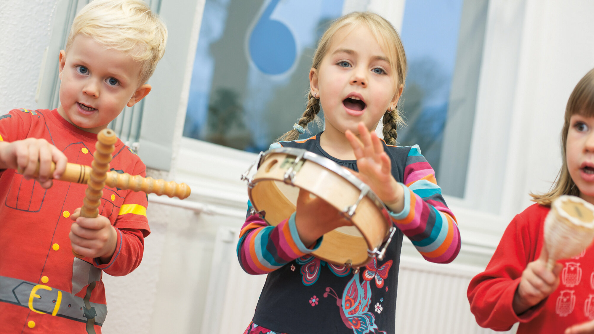 Ein Junge und zwei Mädchen spielen mit Trommel, Rassel und Klanghölzern