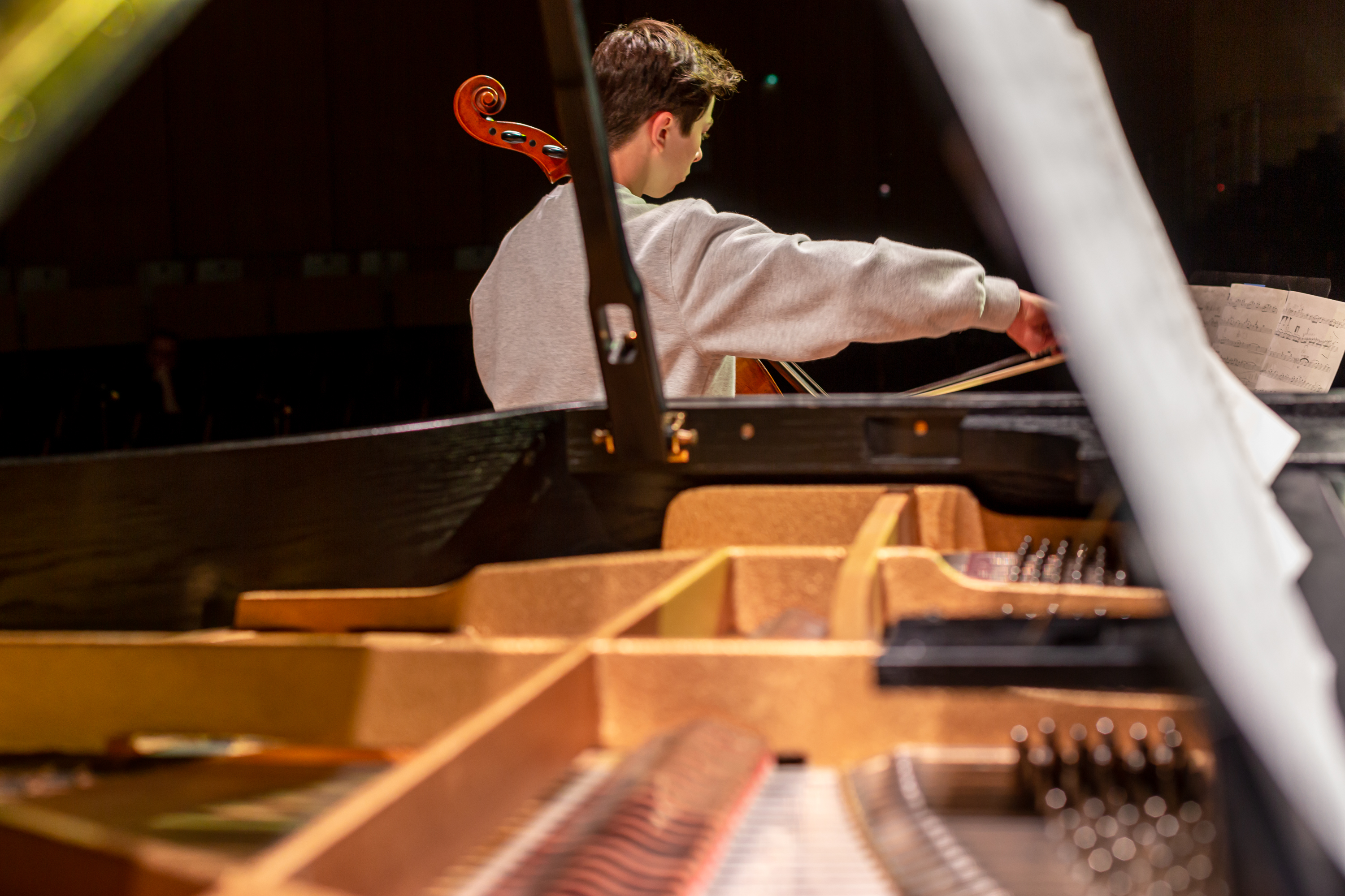Junge spielt hinter einem offenen Flügel Cello