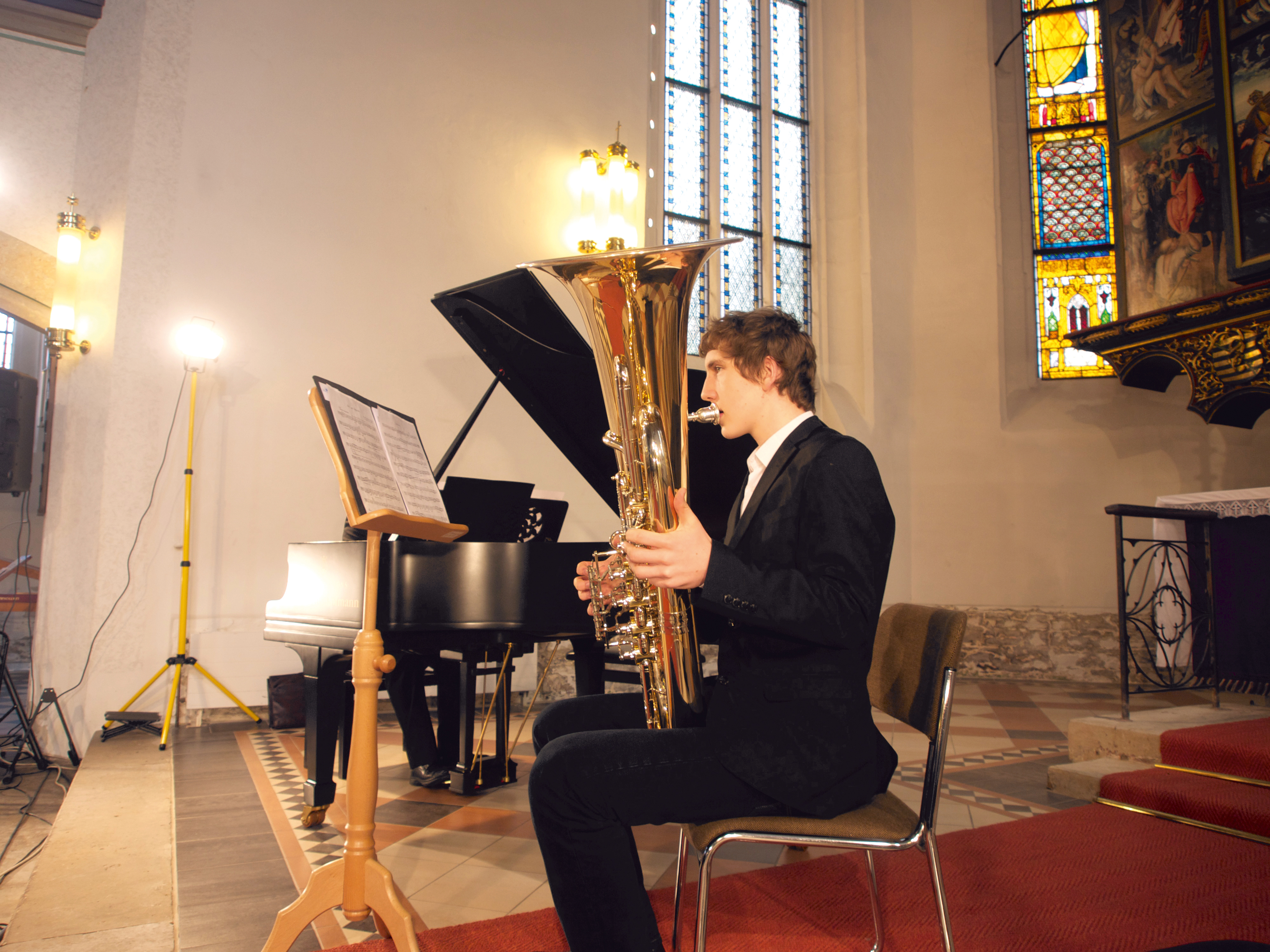 Junger Mann musiziert sitzend mit Tuba in der Kirche 