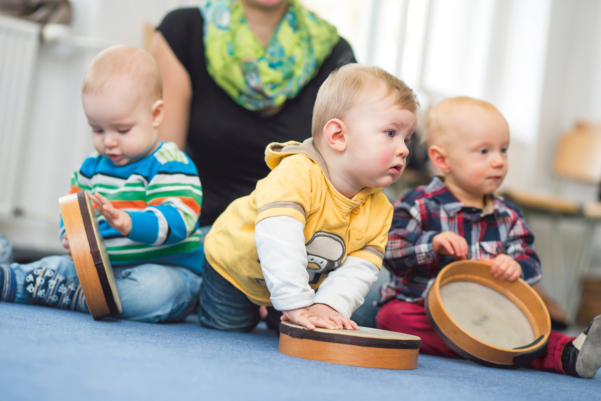 Drei Babies sitzen auf dem Boden und spielen mit Trommeln 