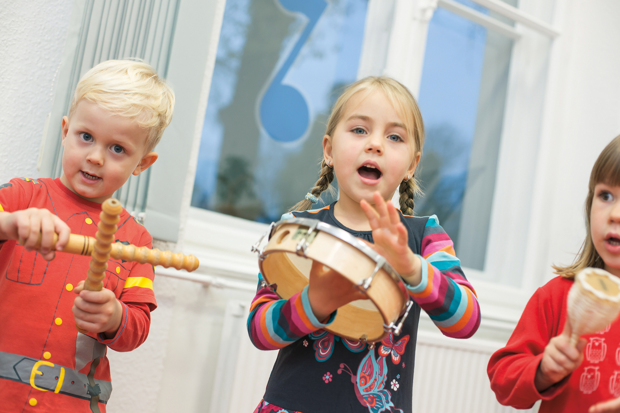 Ein Junge und zwei Mädchen spielen mit Trommel, Rassel und Klanghölzern