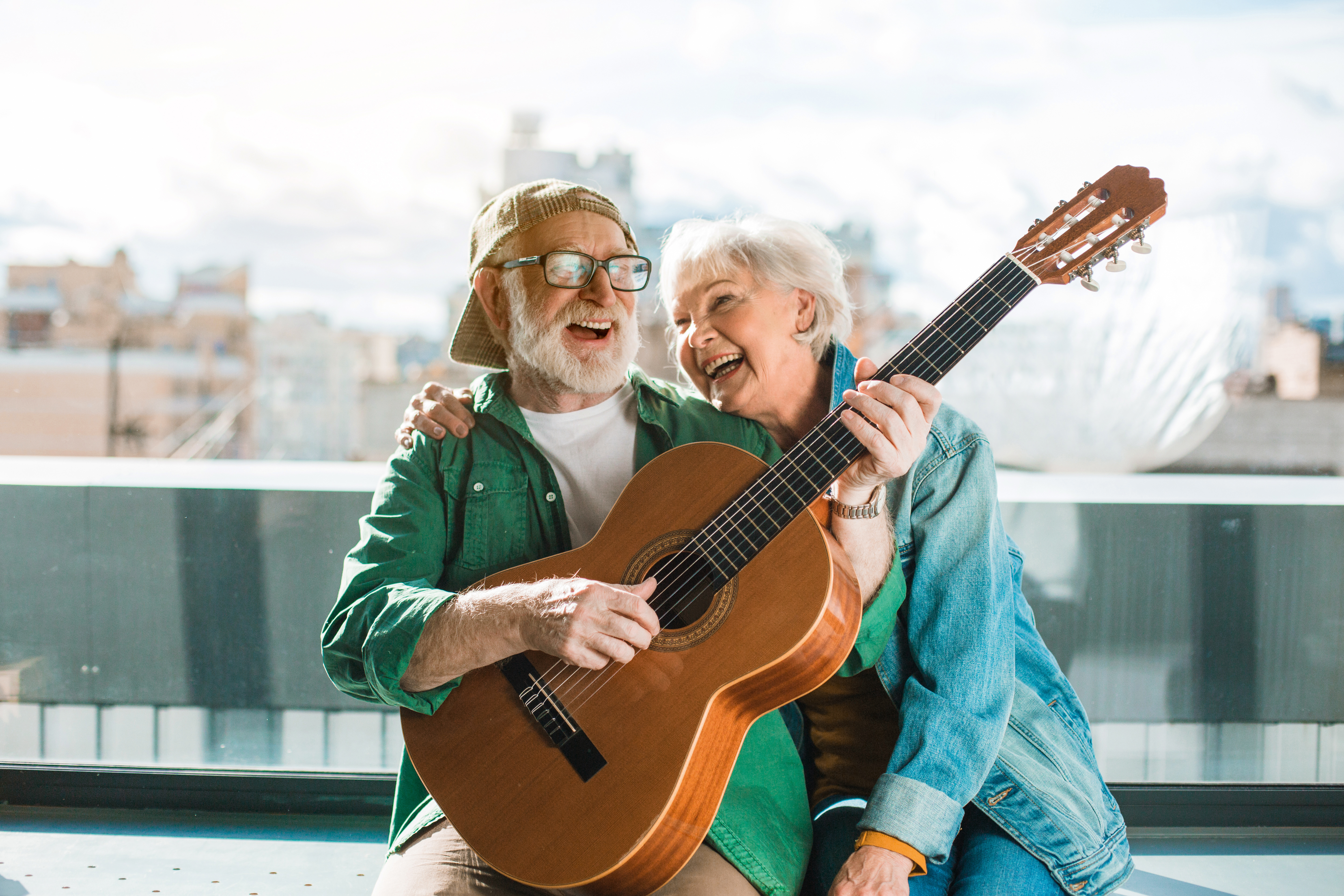 Ein älterer Herr und eine ältere Dame spielen lachend gemeinsam Gitarre