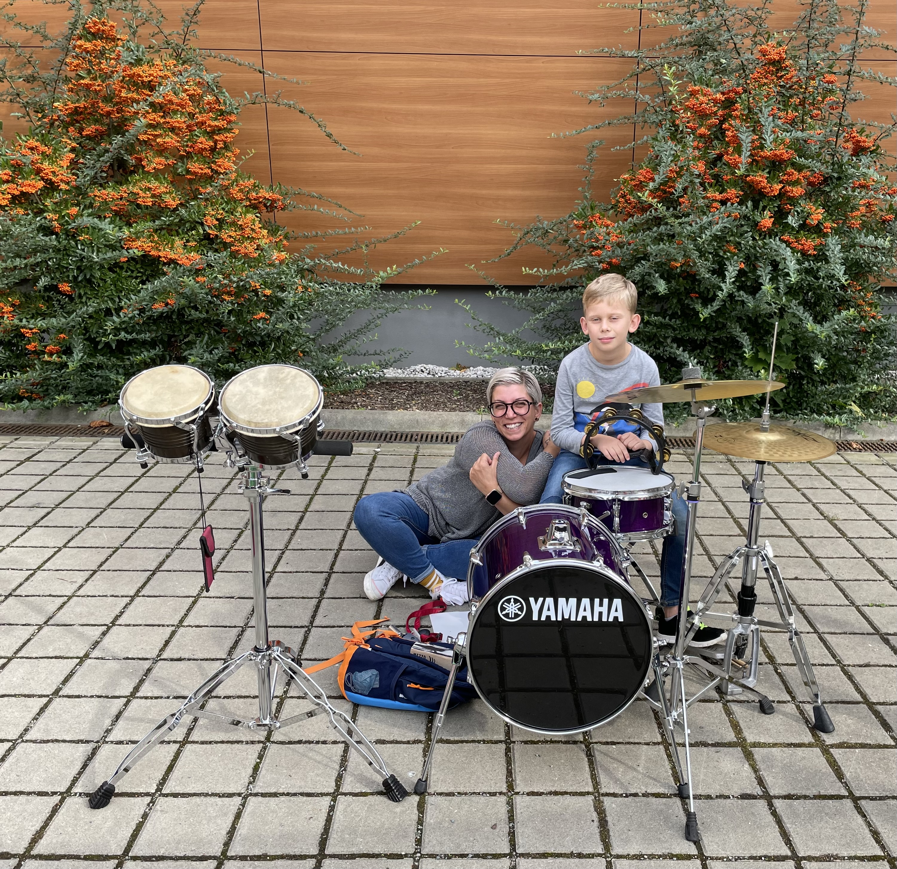 Eine Schlagwerklehrerin posiert mit ihrem Schüler vor einem Schlagzeug und Trommeln