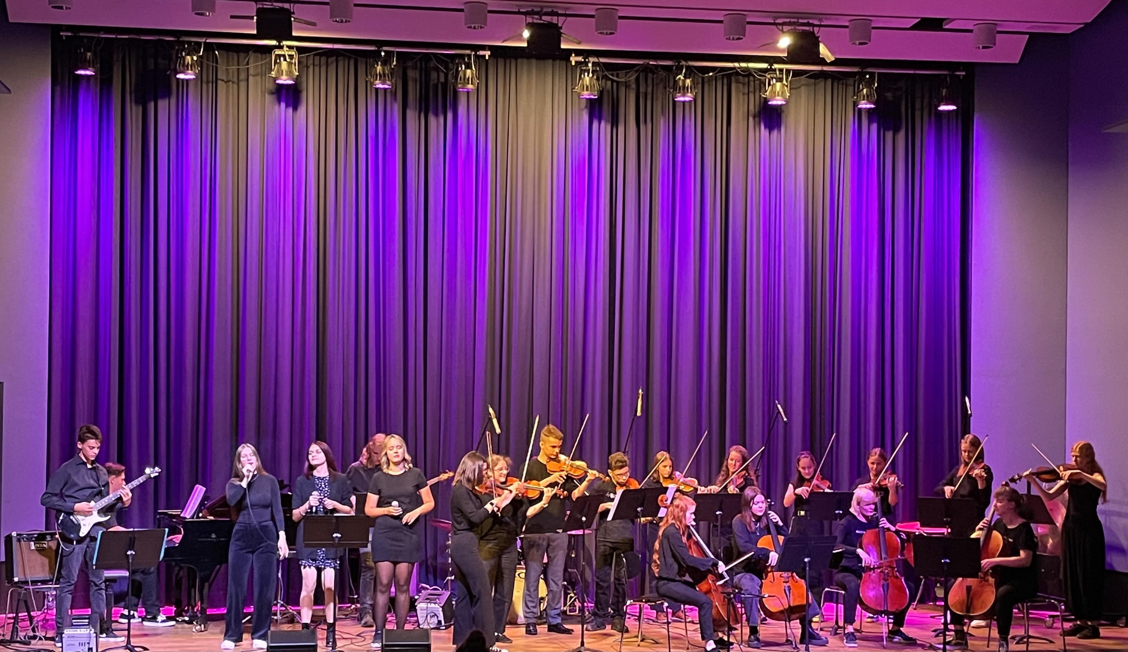 Die Streicherband Rock'n'Strings musiziert im Konzertsaal. Es singen drei Sängerinnen.
