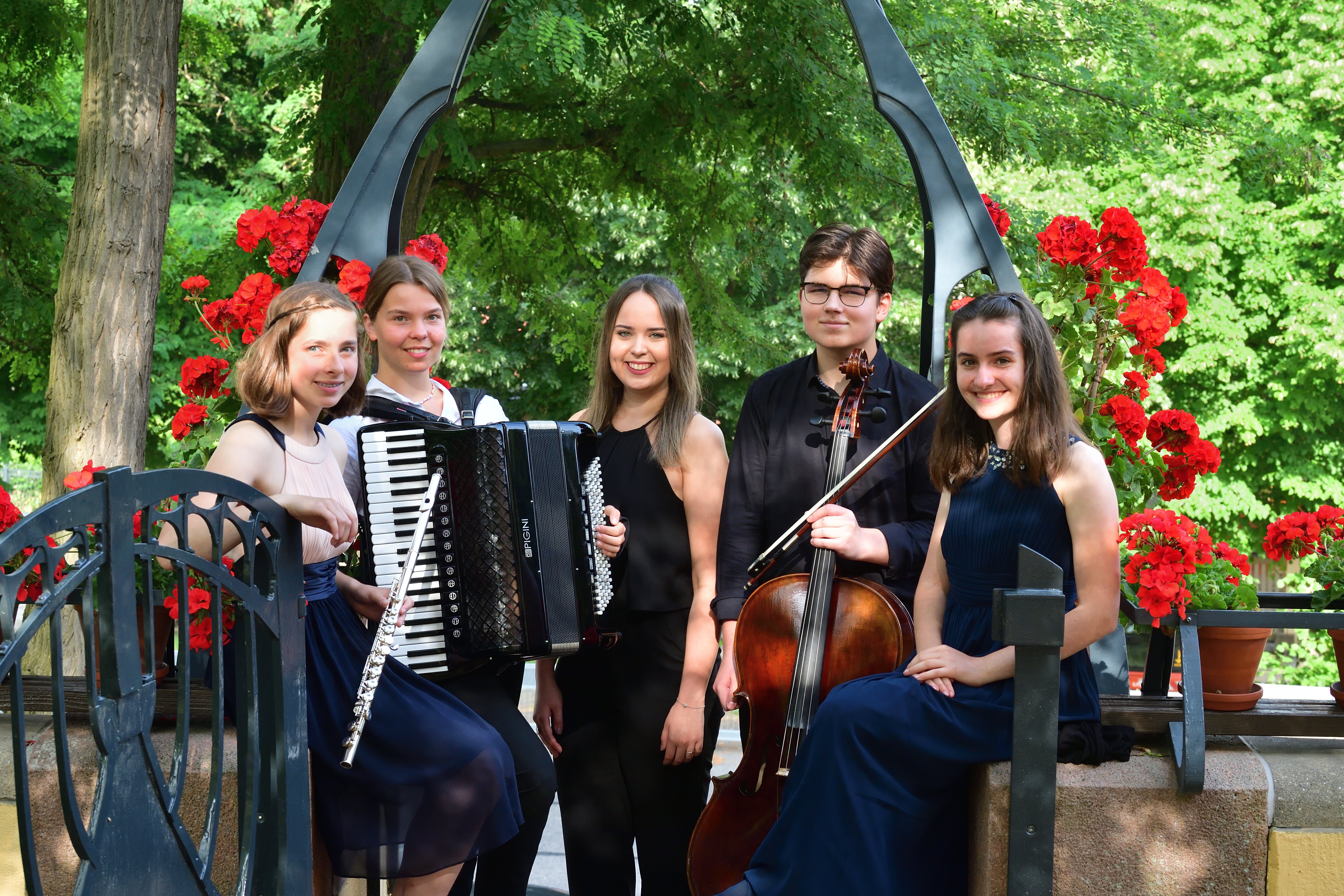 Die Preisträger:innen posieren mit ihren Instrumenten vor einem Blumenbogen